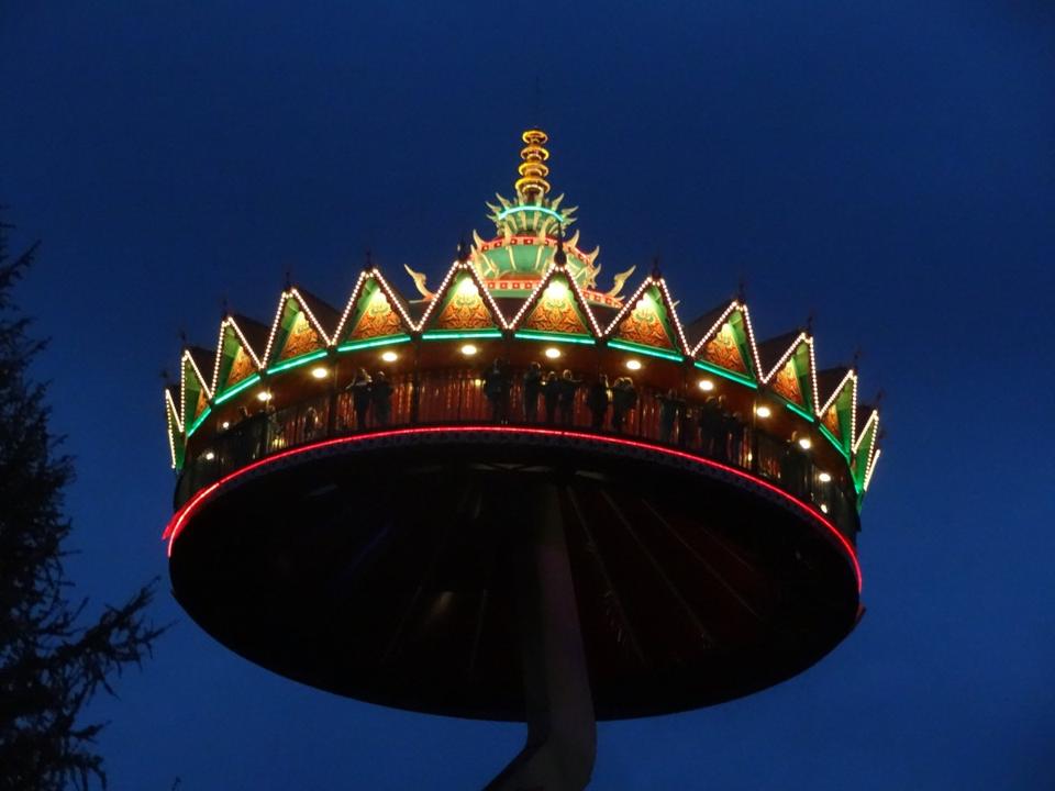 The Pagode ride lit up in green, gold and red against a deep blue evening sky, with riders silhouetted along the rail.