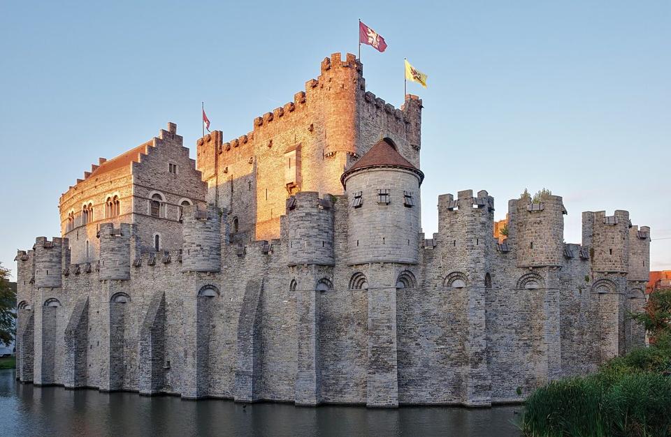 Das Gravensteen, eine von Wasser umgebene Steinburg im Zentrum von Gent, von der Abendsonne beleuchtet.