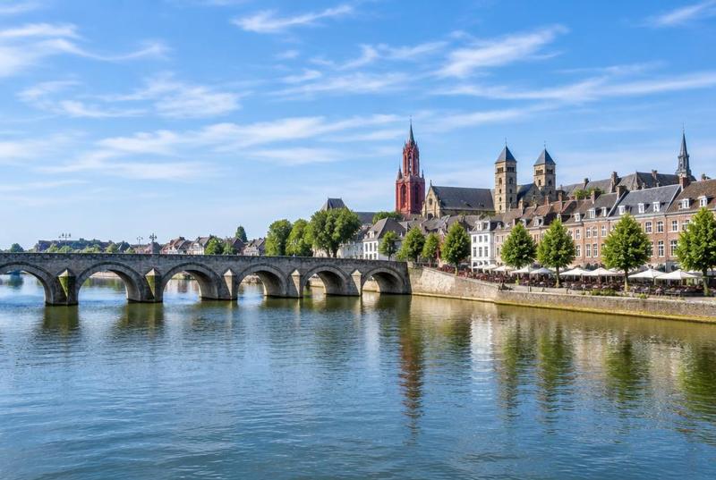 The river Maas at Maastricht, a long arched stone bridge and the old town's towers along the sunlit bank.