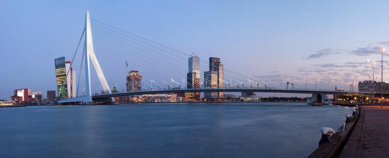 The Erasmus Bridge across the Maas at dusk, with the towers of the Kop van Zuid lit behind it.