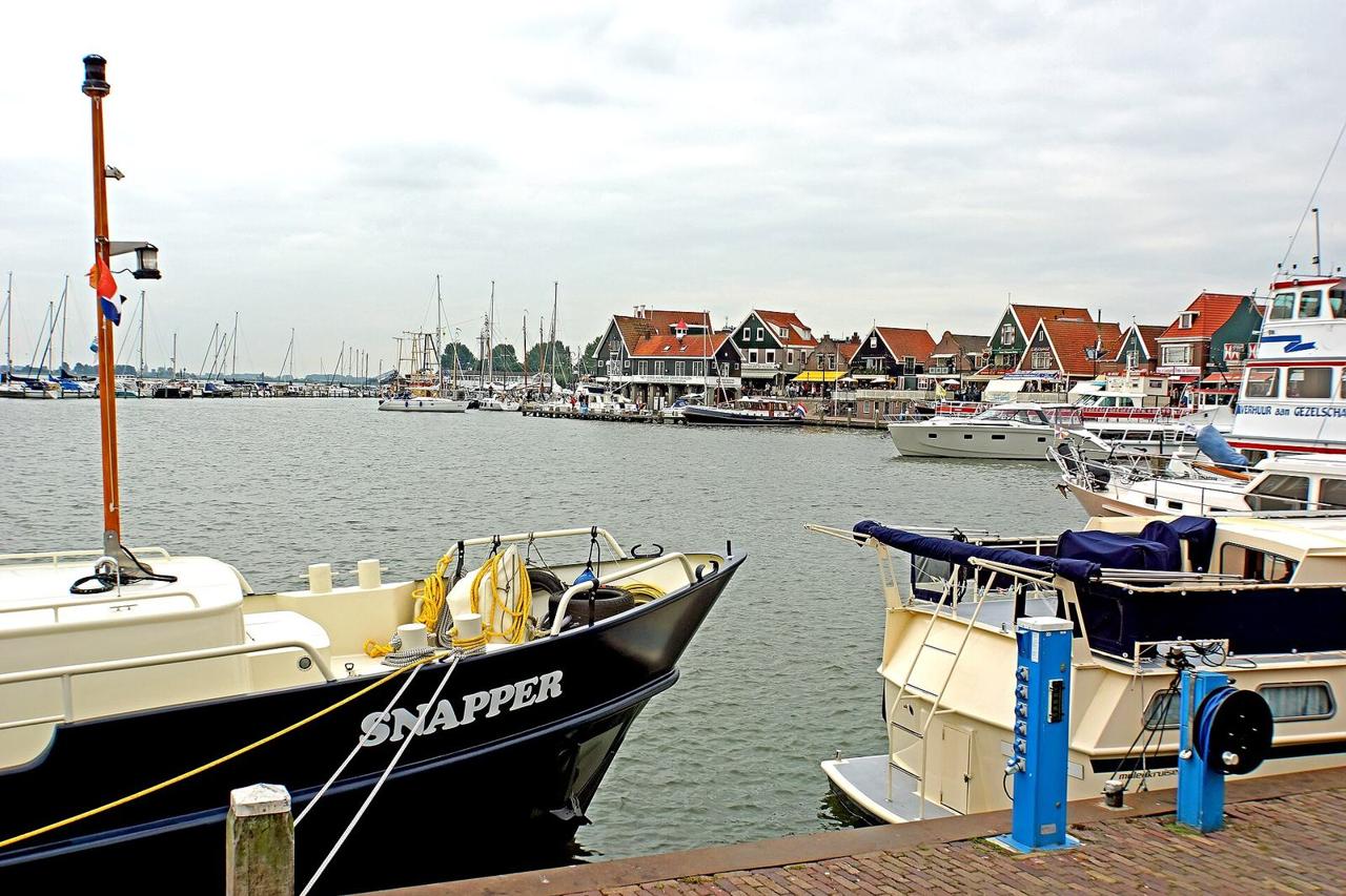 Boote im Hafen von Volendam, dahinter die Reihe der Giebelhäuser aus Holz und die Cafés am gegenüberliegenden Kai.