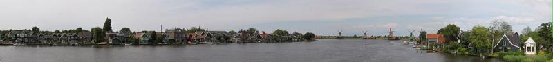 A wide view across the river Zaan at Zaanse Schans, with green wooden houses along one bank and windmills standing against an open sky.