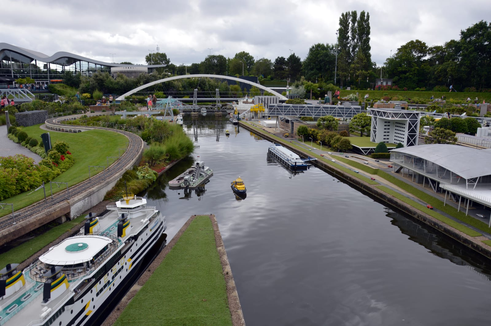 De miniatuurhaven, met modelveerboten en vrachtschepen op echt water naast een terminal op schaal.