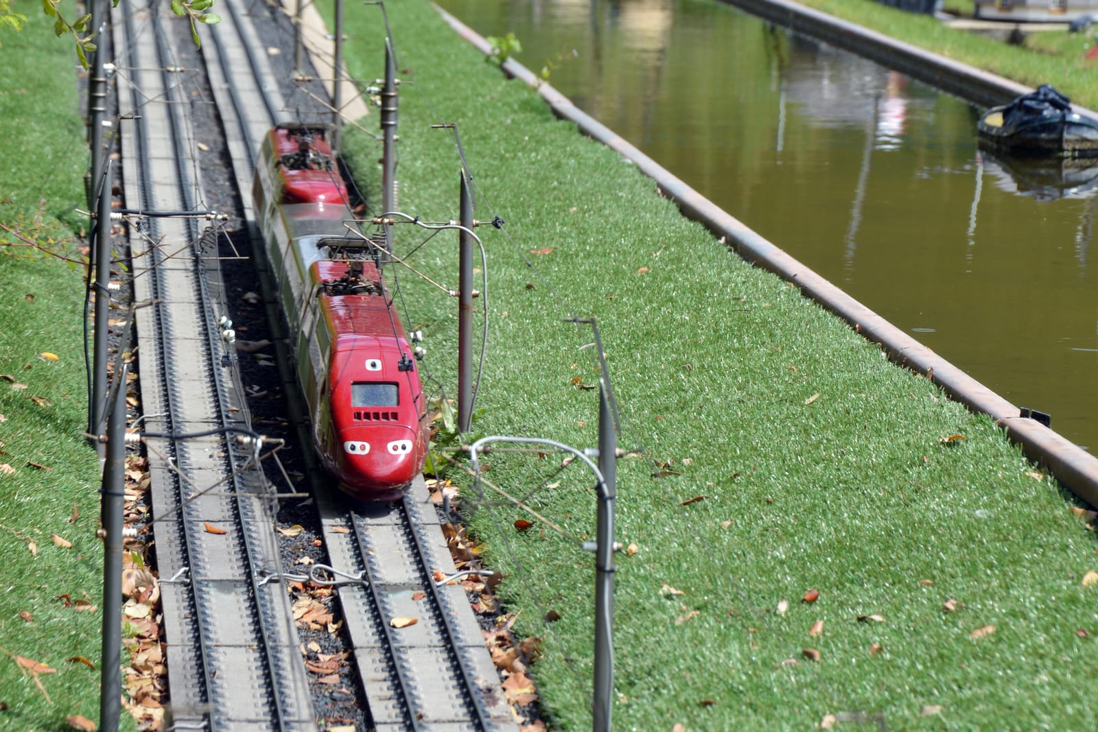 Een hogesnelheidstrein op schaal rijdt over de werkende modelspoorlijn langs een miniatuurkanaal.