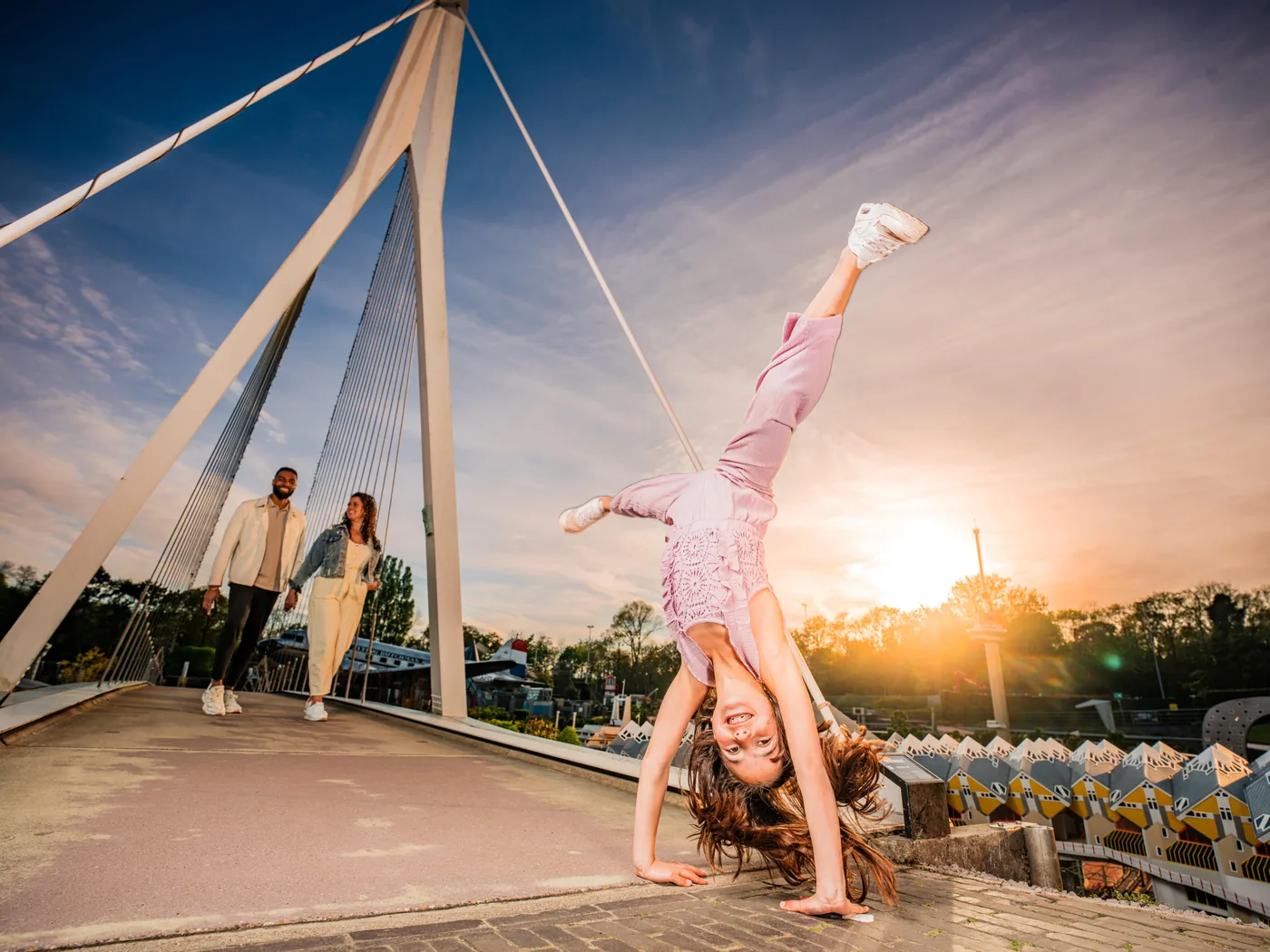 A child doing a cartwheel beside the miniature Erasmus Bridge at sunset.