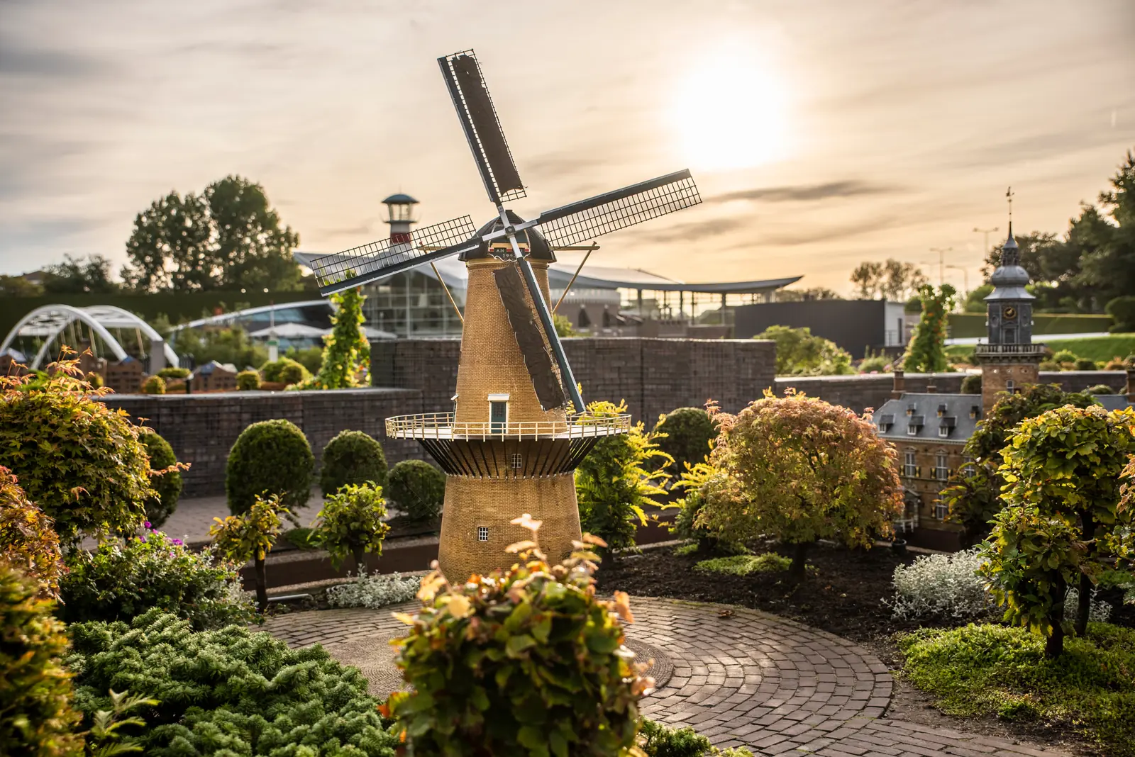 A miniature Dutch windmill among gardens at Madurodam in warm evening light.