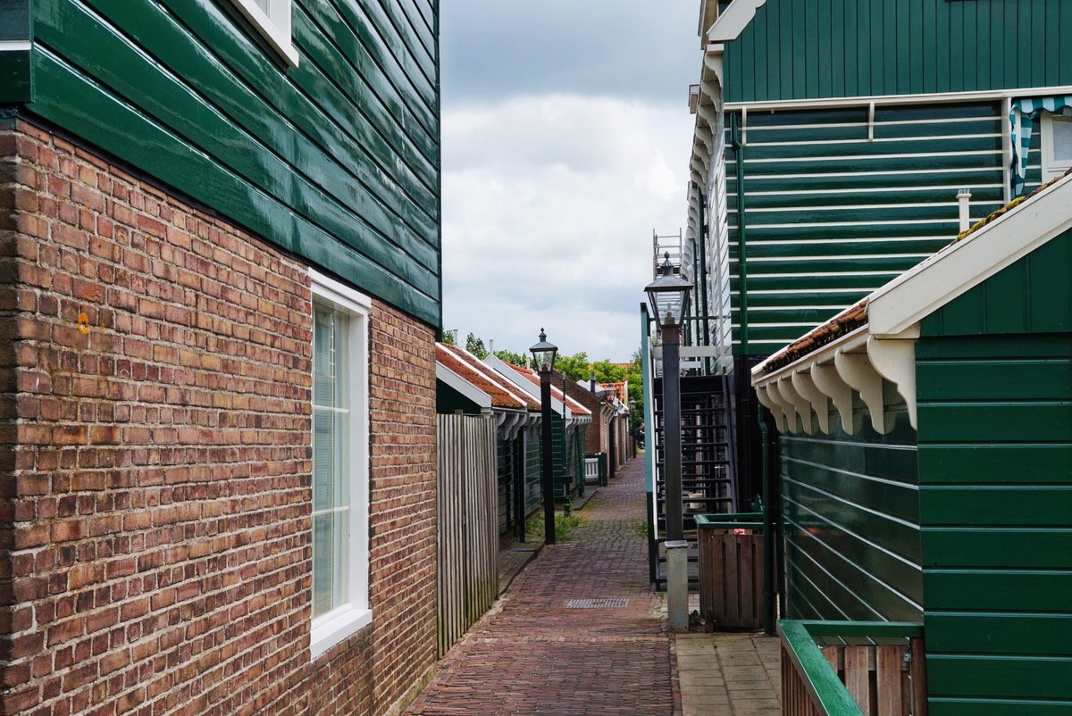 Een smal bakstenen straatje tussen donkergroene houten huizen in het dorp Marken.
