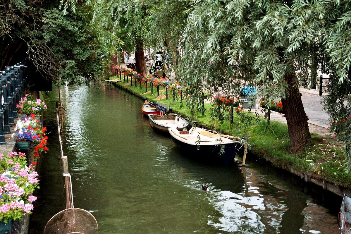 Kleine roeiboten afgemeerd langs een rustige gracht in Monnickendam, met bloemen en wilgen langs de kant.
