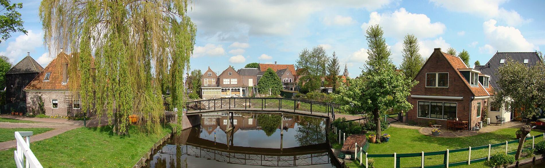 Weids beeld van een gracht in Monnickendam met een voetbrug, treurwilg en bakstenen huizen weerspiegeld in het water.