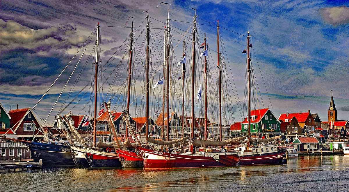 Traditionele houten zeilschepen afgemeerd in de haven van Volendam voor felgekleurde huizen en een kerktoren.