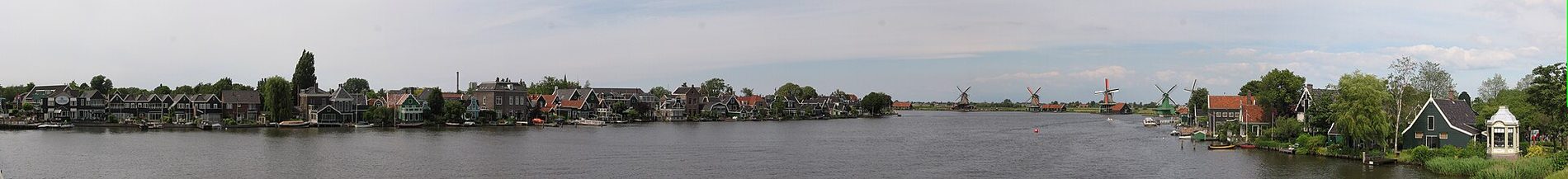 Weids uitzicht over de Zaan, met historische huizen langs de ene oever en de rij molens aan de overkant.
