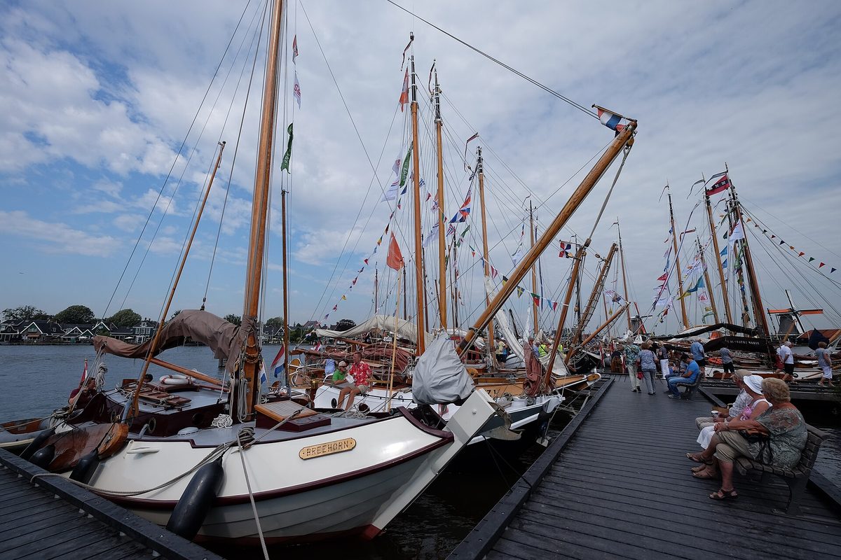 Traditionele platbodems afgemeerd aan een houten steiger aan de Zaan onder een blauwe lucht.